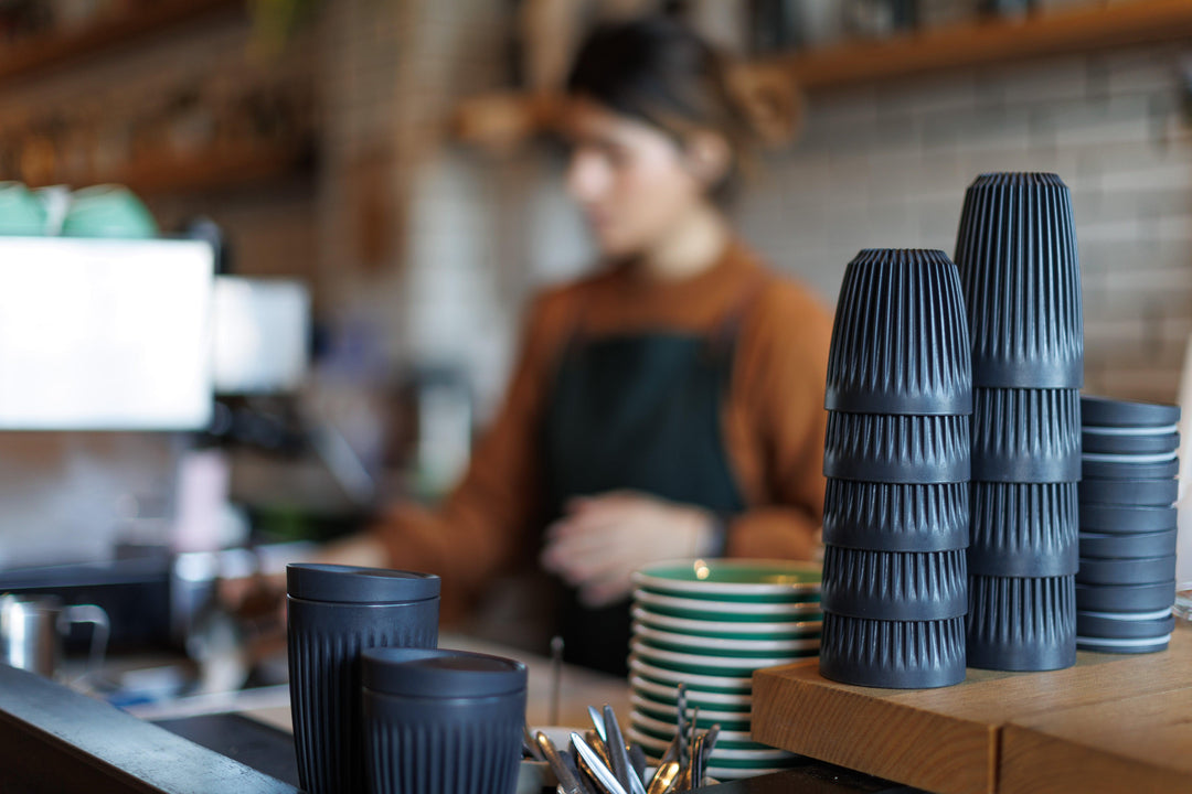 Stacked eco-friendly coffee cups in a cozy cafe setting with barista in background