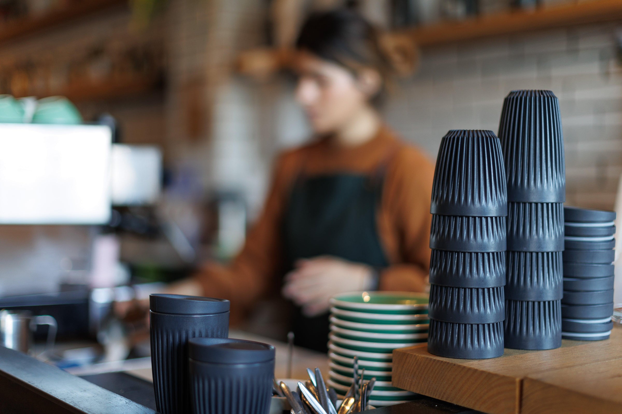 Stacked eco-friendly coffee cups in a cozy cafe setting with barista in background