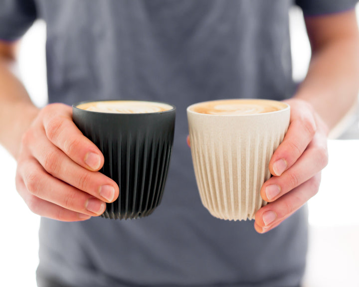 Hands holding charcoal and natural HuskeeCups